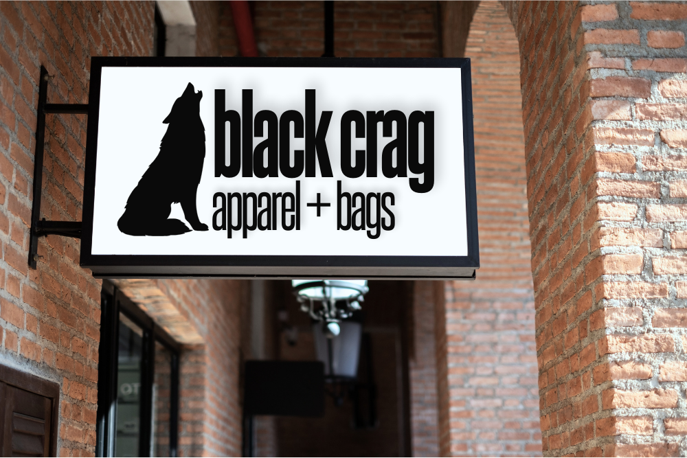 A sign hanging off a brick storefront featuring the Black Crag logo
